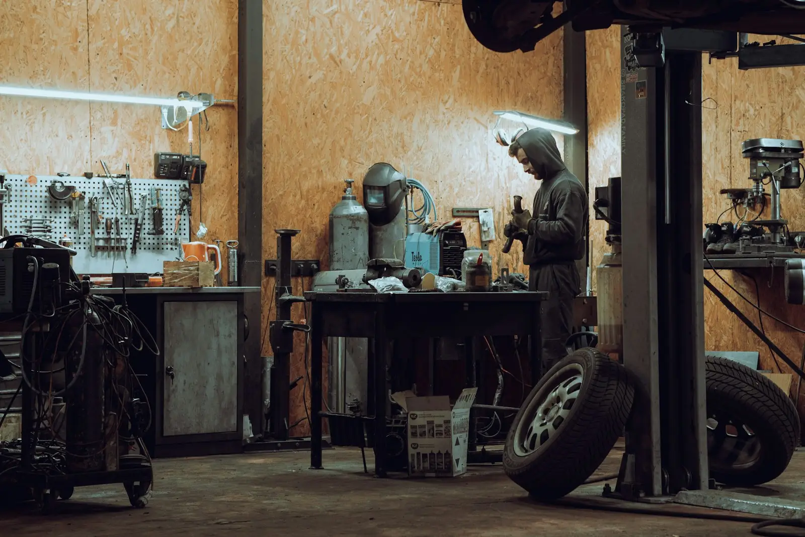 Mechanic at the workbench in a repair shop, with tires and a lift