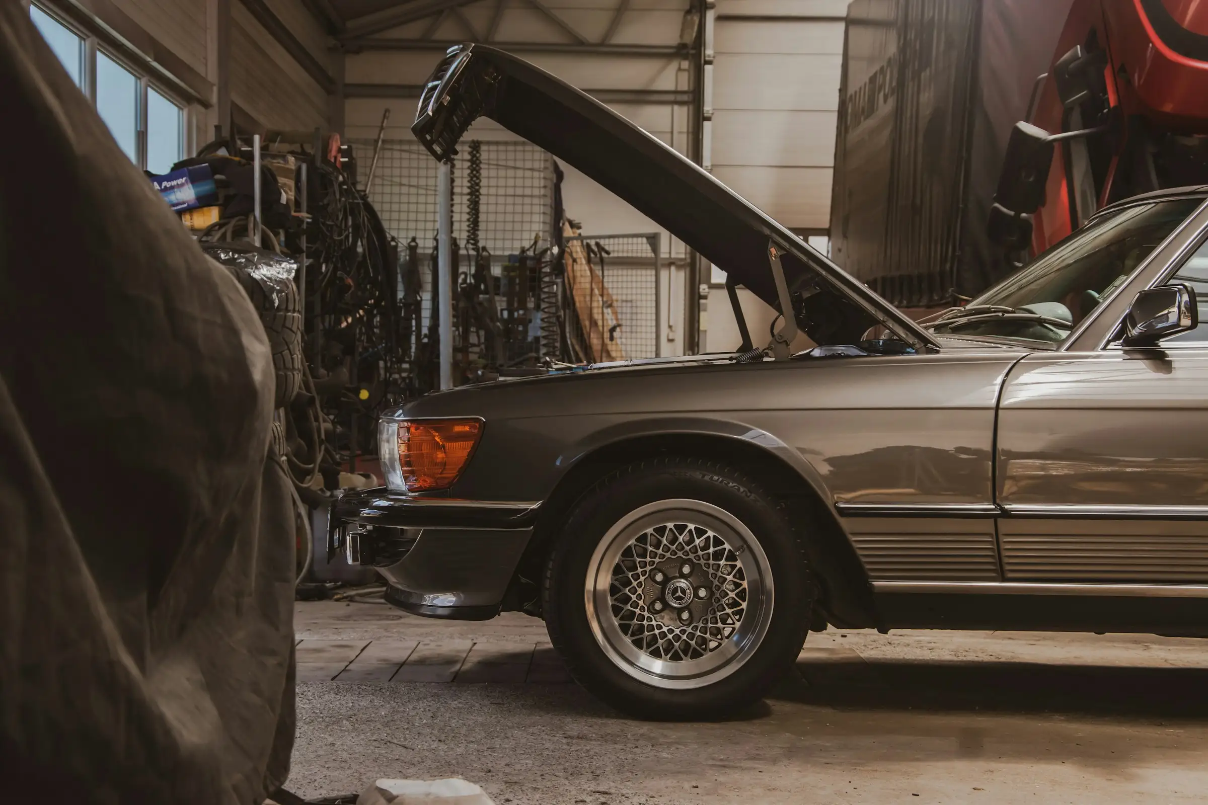 A classic Mercedes-Benz SL with its hood up in a repair shop